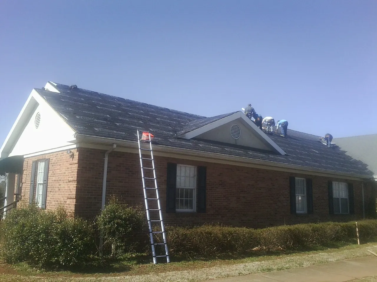 Crew tearing shingles off a brick ranch roof with a ladder set — Metal Roof Repair work by our crew in Laurel Hill