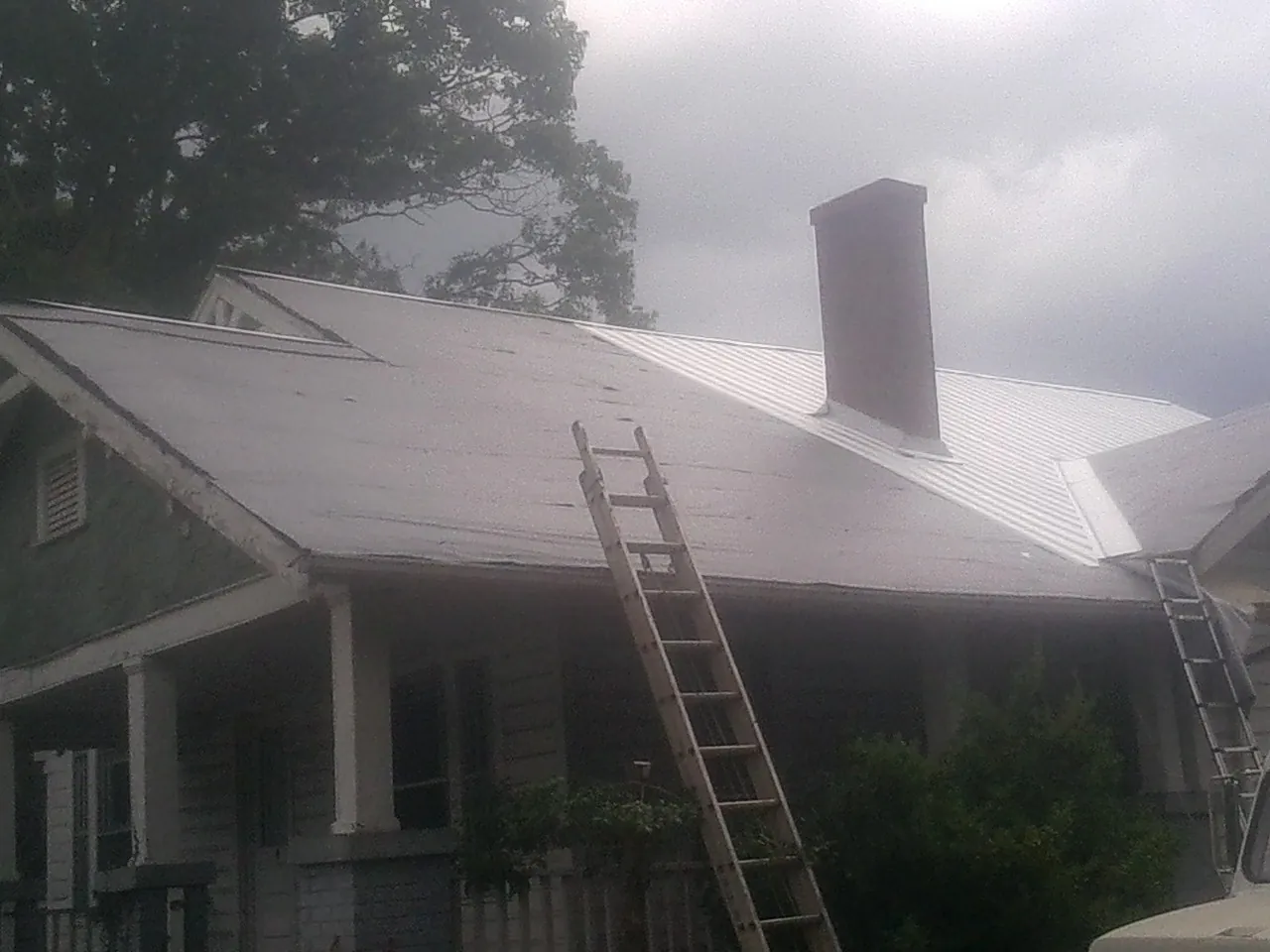 Ladders against a metal roof on an older home with a brick chimney in Laurel Hill