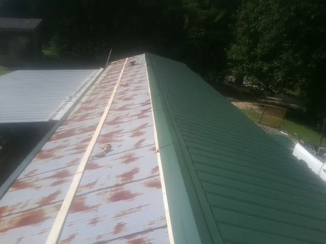 Old rusted panels beside newly installed green metal roofing — Wind Damage Roof Repair by Roofing Brothers in Laurel Hill