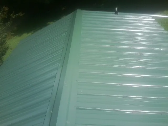 New green metal panels meeting at the ridge of a roof — Flat Roof Repair work by our crew in Laurel Hill