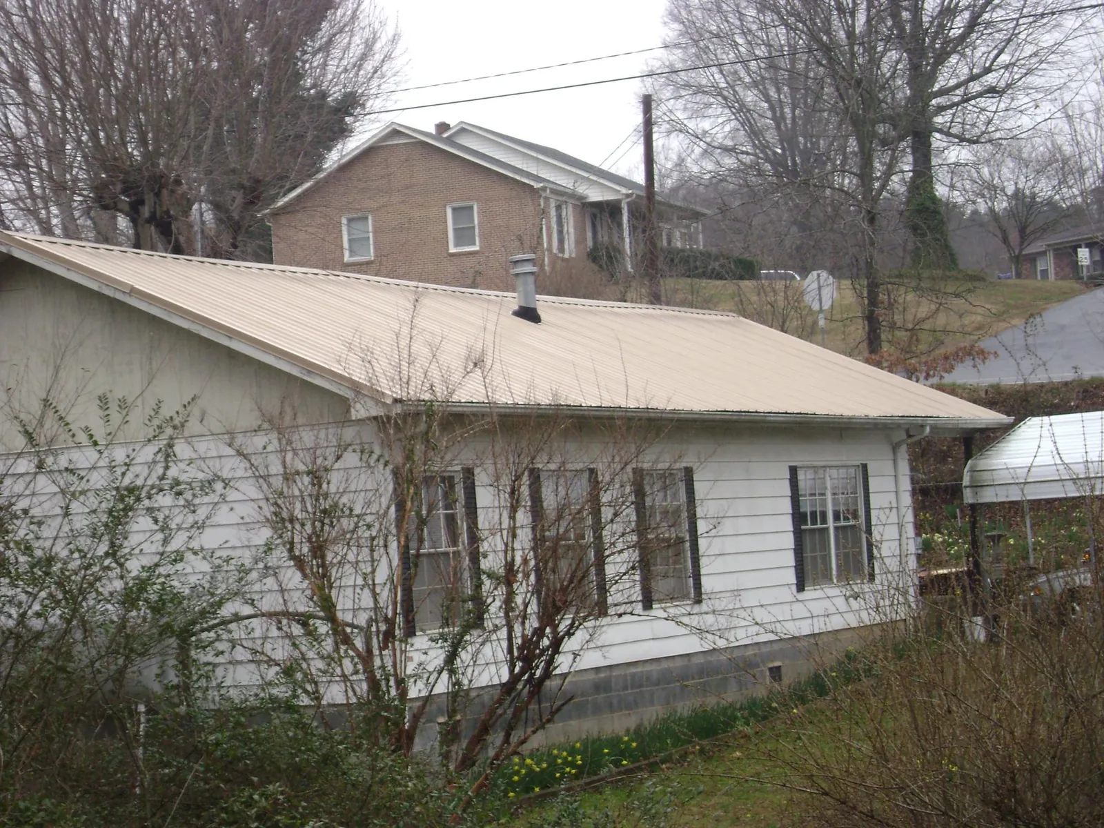Tan metal roof on a white sided house set into a hillside — Commercial Roofing by Roofing Brothers in Laurel Hill