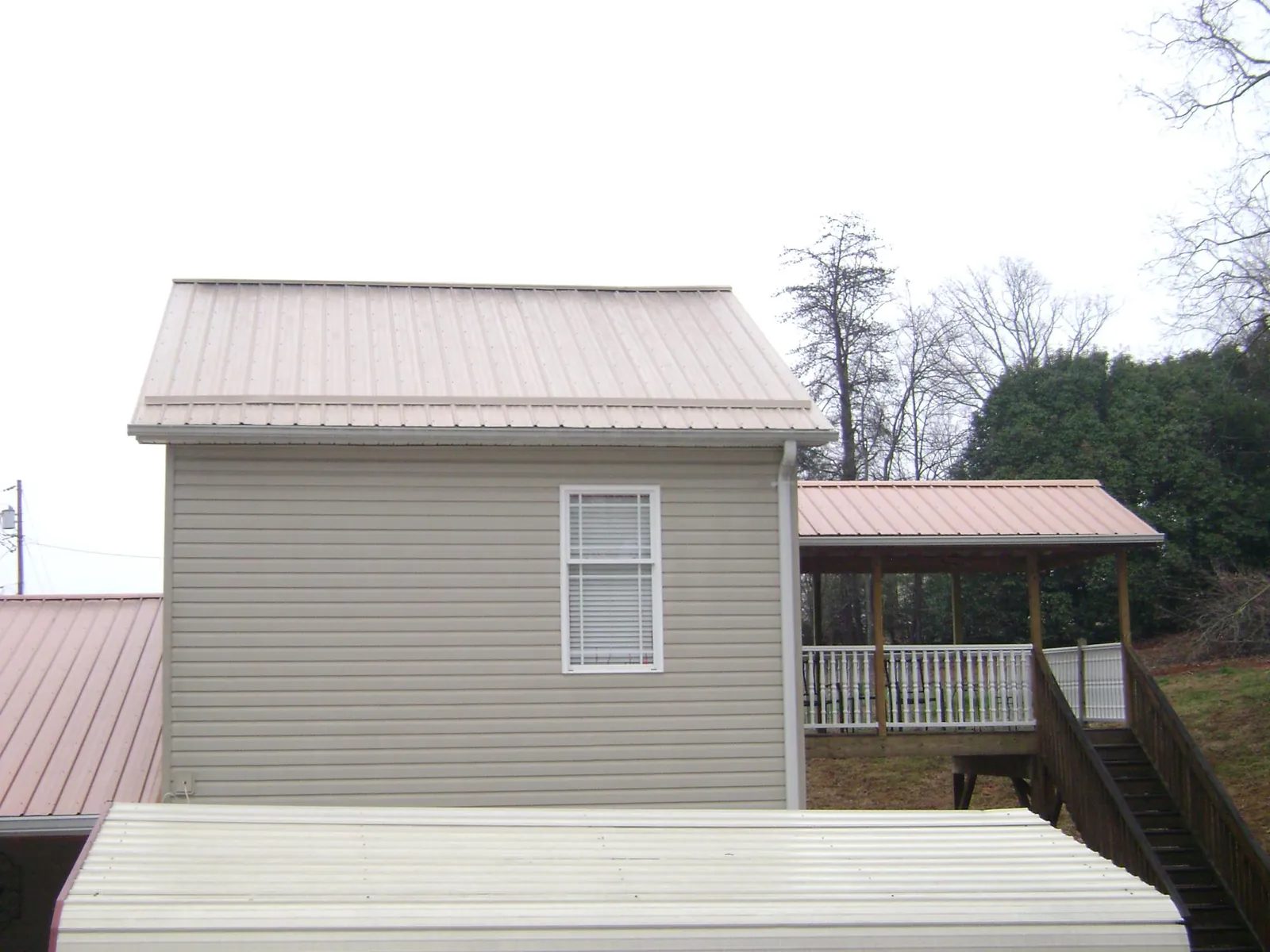 Tan metal roofs on a two story addition and attached porch, from a Roof Replacement job in Laurel Hill